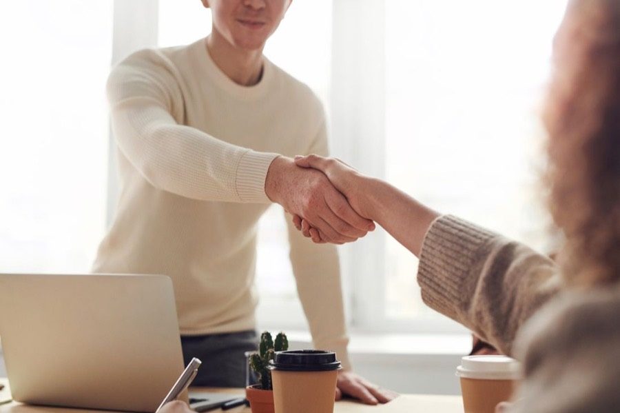 Two people shaking hands across a desk after a meeting.